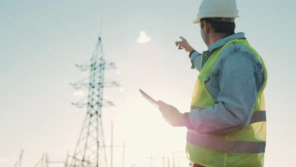 Engineer Standing on Field with Electricity Towers