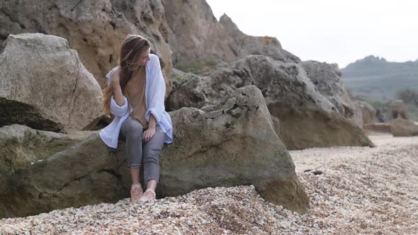 A Young Woman Sits on a Rock and Looks at the Sea