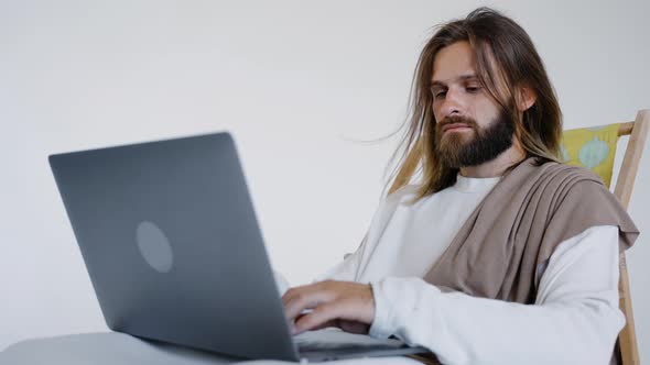 Jesus Sits in a Schizlong and Works at a Computer on a White Background alt