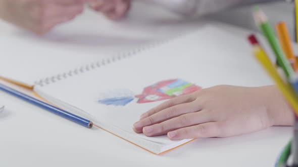 Close-up of Caucasian Child's Hands Drawing with Colorful Pencil in Exercise Book