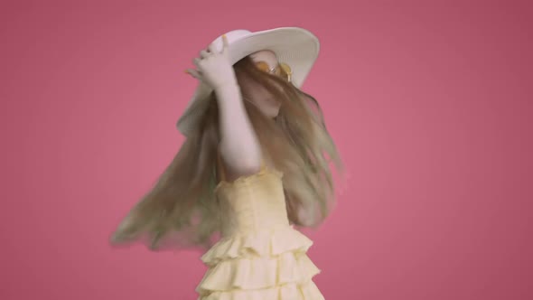 Child Girl in Yellow Dress and Hat is Dancing Ang Singing on Pink Background