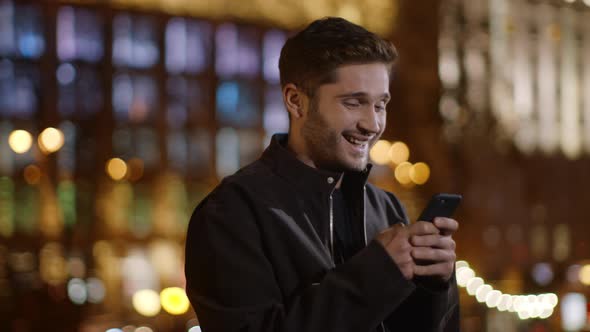 Excited Guy Messaging Mobile Phone on Street. Cheerful Man Using Phone Outdoors.