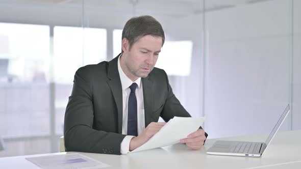 Middle Aged Businessman Reading Documents in Office