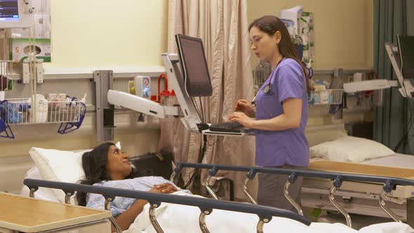 Modern nurse assesses and talks with female patient and uses computer.
