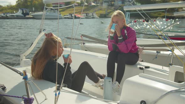 Two Young Athletes During a Break in the Regatta Drink Coffee and Communicate on the Internet on