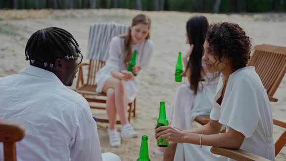 Young People Chatting and Drinking Sitting at the Campfire at the Beach