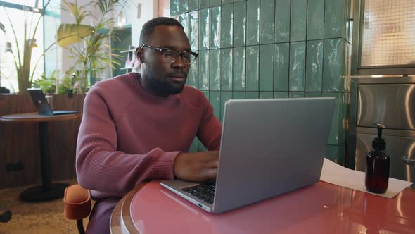 Young Black Man Working Remotely on Laptop in Cafe