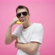 A man is dancing with a banana phone. In a white T-shirt on a pink background, in black sunglasses. - VideoHive Item for Sale