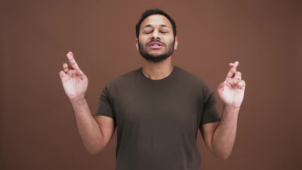 Emotional Indian Man Praying to God Asking for with with Crossed Fingers and Enjoying Success Brown