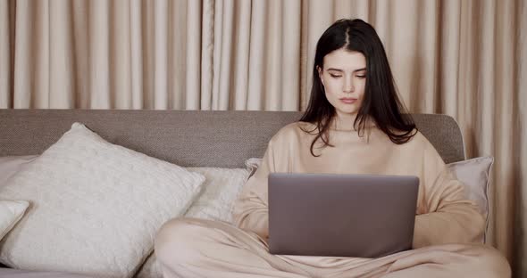 Attractive Woman Typing on Keyboard Working with Laptop Computer in Bedroom