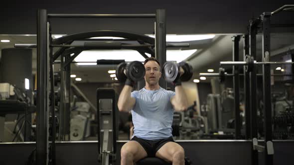 Muscular man holding dumbbell above the head at the gym.