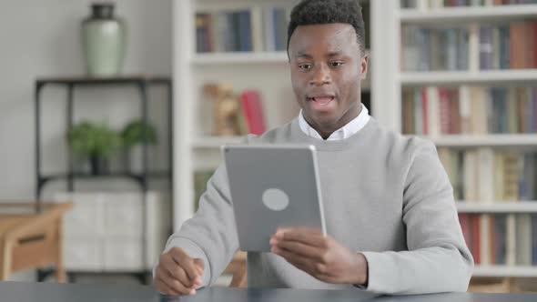 African Man Making Video Call on Tablet in Library