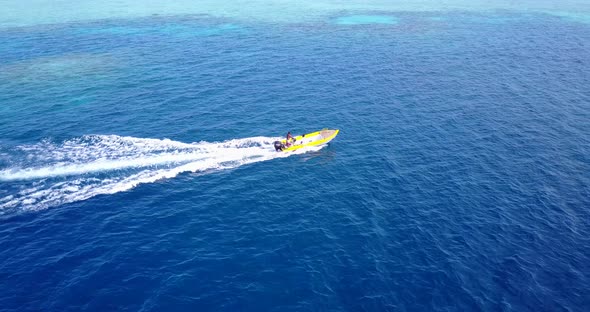 Yellow speed boat tracing across deep blue sea and azure shallow waters on a shiny day near seashore