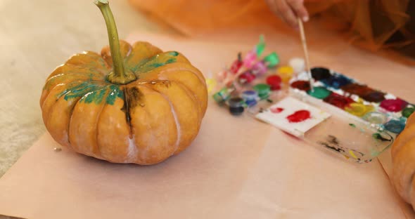 Little girl drawing face on orange Halloween pumpkin