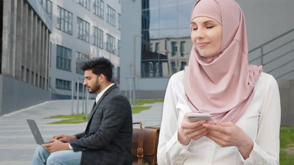 Muslim Woman Using Smartphone While Man Working on Laptop