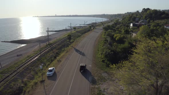 Aerial Shot Flying Over Nature Seascape with Suv Automobile Driving on Asphalt Highway at Sunset