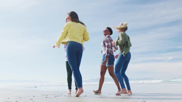 Happy group of diverse female friends having fun, dancing and smiling at the beach