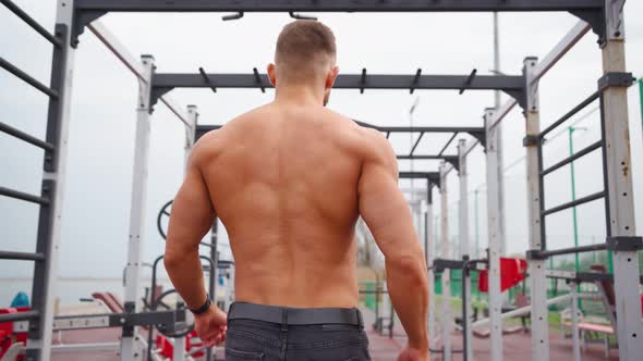 Muscular Man Naked Torso Walks Along Horizontal Bars and Bowls on Sports Ground