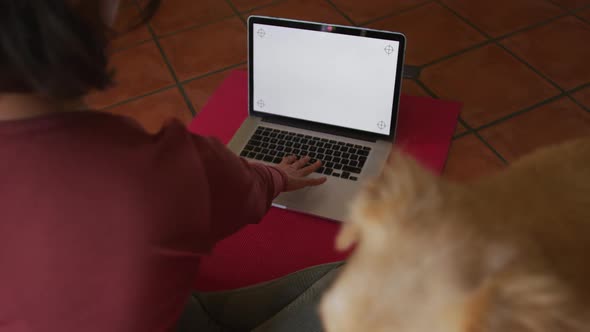 Caucasian woman practicing yoga with her pet dog using laptop with blank screen at home
