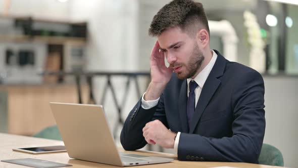Stressed Young Businessman with Laptop Having Headache in Office