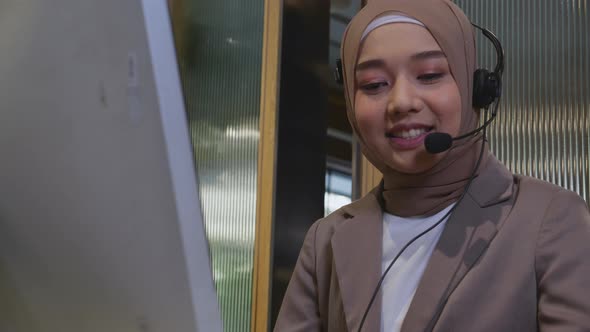 Young asian woman is muslim wearing headset working call center and looking document at office.