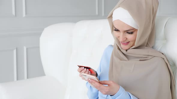 Muslim Woman in Hijab Is Buying Online with a Credit Card and Smartphone.