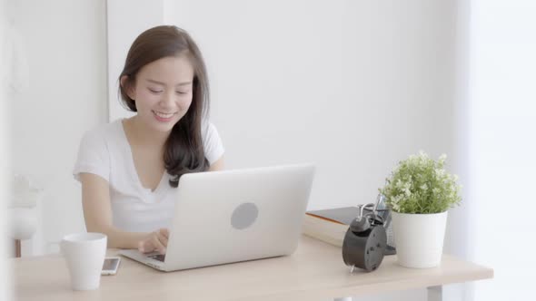 Beautiful young freelance asian woman smiling working and typing on laptop computer at desk.
