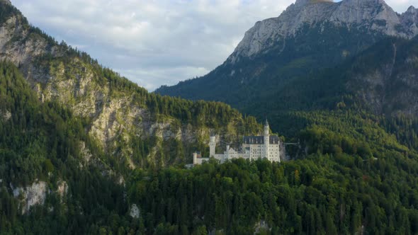 Perfect white castle in the middle of the mountains, surrounded by forest trees. Static aerial shot,