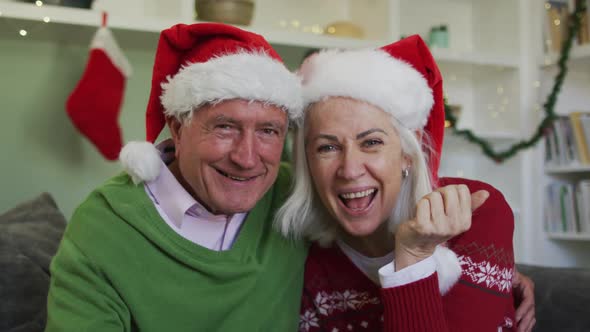 Portrait of happy senior caucasian couple celebrating christmas wearing santa hats