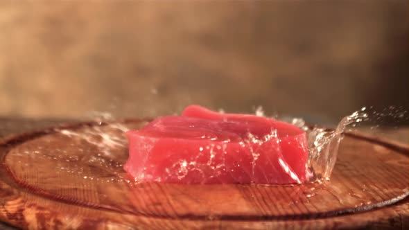 Super Slow Motion on a Wooden Cutting Board Falls Raw Tuna Steak with Spray