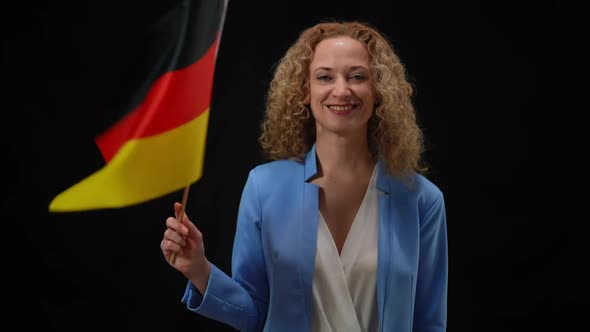 Confident Smiling Elegant Woman Fluttering German Flag Looking at Camera in Camera Flashes at Black