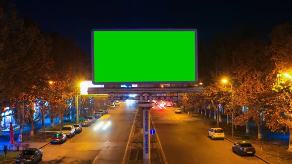 A Billboard with Green Chroma Key on a Background of a City Night Landscape of Fast Moving Cars with