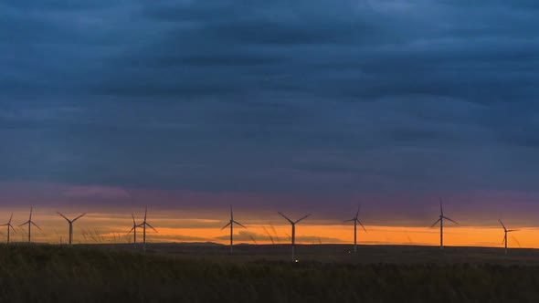 Motion the Blades of a Large Wind Turbine in a Field Against a Background of Orange Sunset on the