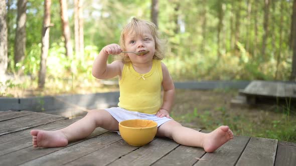 Little Funny Cute Blonde Girl Child Toddler with Dirty Clothes and Face Eating Baby Food Fruit or