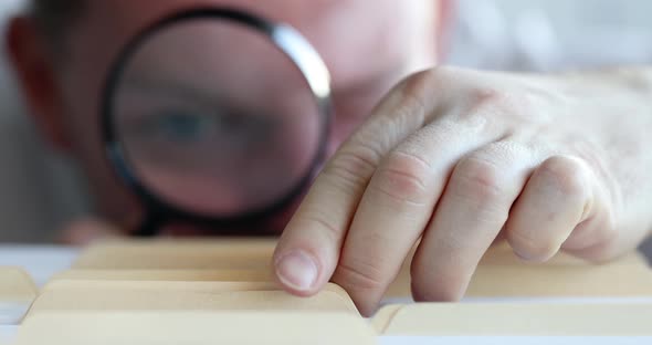 Employee Looks Through Magnifying Glass and Searches for Required Document