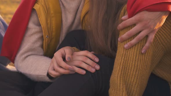 Guy and Girl Join Hands Sitting at Bonfire in Camp Closeup