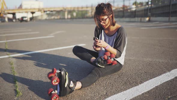 Attractive Hipster Female Fix Roller Skates on the Street at Sunset