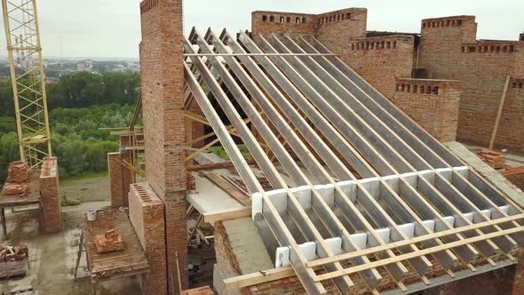 Aerial view of unfinished brick apartment building with wooden roof structure under construction.