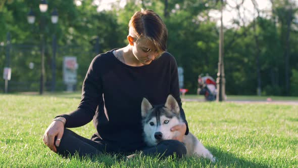 Beautiful Young Woman Playing with Funny Husky Dog Outdoors in Park