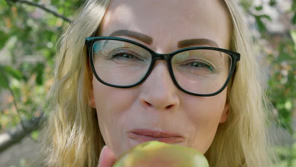 portrait of a young woman biting and eating a ripe green apple, looking at the camera in the garden