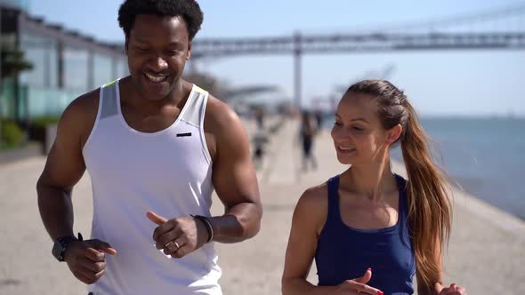 Happy Sporty Young Couple Jogging Along Embankment