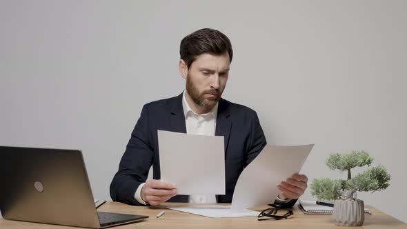 Bearded caucasian man wearing formal wear sitting at the table and examining documents