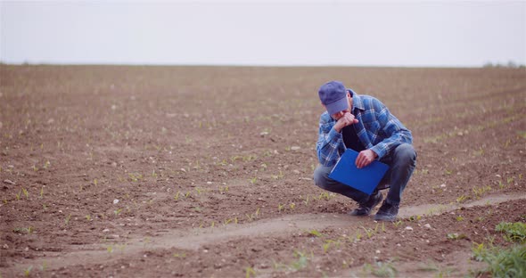 Thoughtful Male Botanist Examining Agriculture Field Plants While Writing On Clipboard