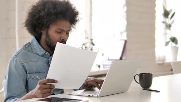 Creative African Man Reading Documents and Working On Laptop