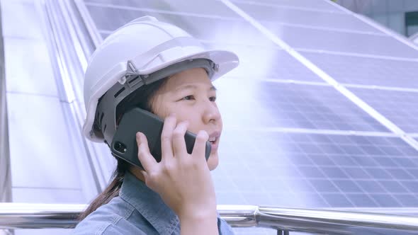 Asian female engineer talking on a phone, smiling near solar panels concept.