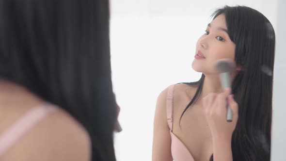 Young asian woman happy and smile with face looking mirror applying makeup with brusher of cheek.