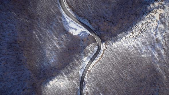 Aerial view of a car road surrounded by snow and trees in Greece.