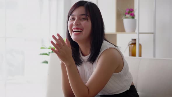 Asian woman happy laughing on indoor sofa at home in casual dress on morning