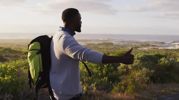 African american man with backpack trying to hitch a lift while standing on the road