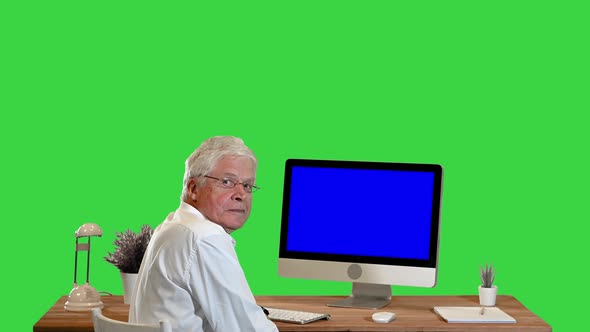 Old Businessman Sitting at the Table with Blank Screen Pc and Talking To Camera Mockup Display on a